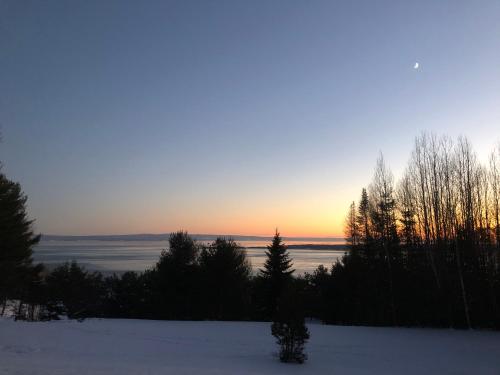 a sunset over a snow covered field with trees at Chalet Sous Les Pins in Les Éboulements