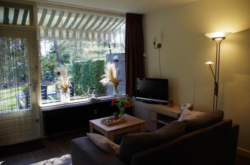 a living room with a couch and a tv and a window at Geschakelde bungalow op de Veluwe "De Eekhoorn" in Otterlo