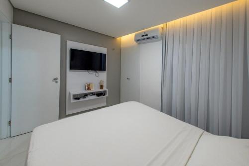 a white bedroom with a white bed and a television at 507 Lindo Flat mobiliado na Praia de Iracema in Fortaleza