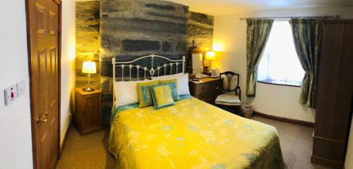 a bedroom with a yellow bed with a stone wall at Yr Hen Fecws in Porthmadog