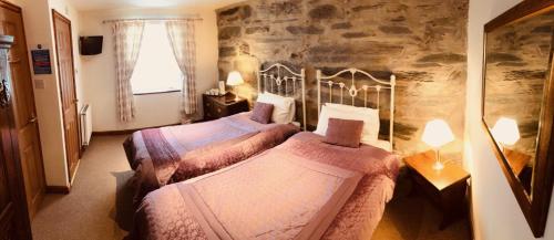 two beds in a room with a stone wall at Yr Hen Fecws in Porthmadog