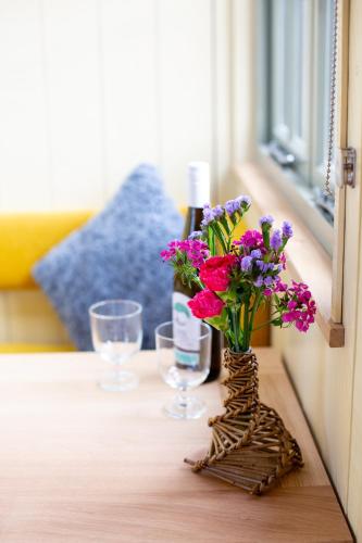 a table with a vase of flowers and wine glasses at Little Plovers Shepherd Hut in Chichester