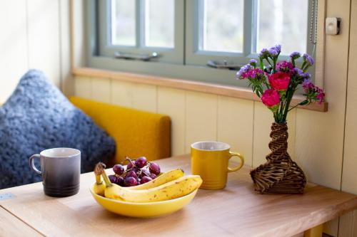 a table with a bowl of fruit and a vase of flowers at Little Plovers Shepherd Hut in Chichester