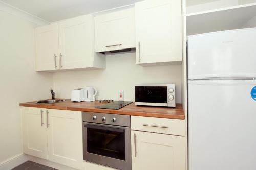 a kitchen with white cabinets and a white refrigerator at Harry Clarke Mews at the Castle Hotel in Dublin