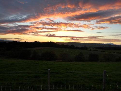 a sunset in a field with a fence at Cleeves Cabins Arran Luxury Lodge with hot tub in Dalry