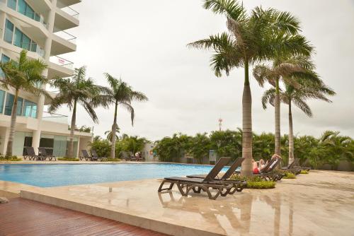 a woman sitting in lounge chairs next to a swimming pool at MODERN 3 ALCOBAS APARTMENT in Cartagena de Indias