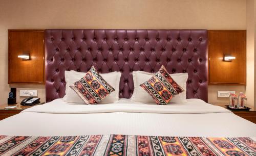 a large bed with a purple headboard and pillows at SK Lords Inn Ahmedabad in Ahmedabad