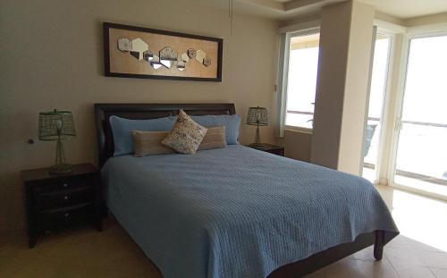 a bedroom with a bed with blue sheets and two windows at Playa Bonita condo in Rosarito