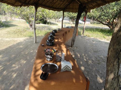 a long wooden bench with a row of drinks on it at Camp Hornbill Corbett in Rāmnagar