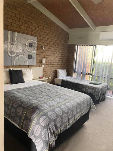 a bedroom with two beds and a brick wall at Baronga Motor Inn in Colac