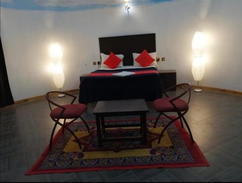 a bedroom with a bed with red pillows and two chairs at Le Apex Inn in Auroville