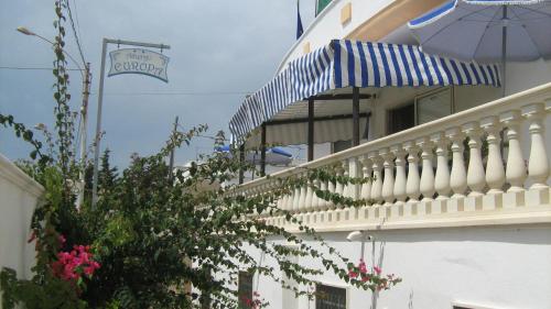 a white building with a balcony with a blue and white umbrella at Albergo Europa in Marina di Mancaversa