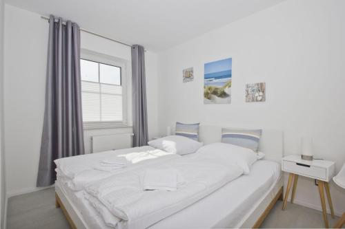 a white bedroom with a large bed and a window at modernen Ferienwohnung mit eigener Terrasse - Haus Inselwind FeWo MEERküste in Groß Zicker