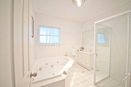 Baño blanco con bañera y lavamanos en Encounter Hideaway Cottages, en Encounter Bay