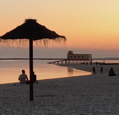 a man sitting under an umbrella on the beach at Fuseta Apartments - Bela Vista & Vista Mar - Penthouses in Fuzeta