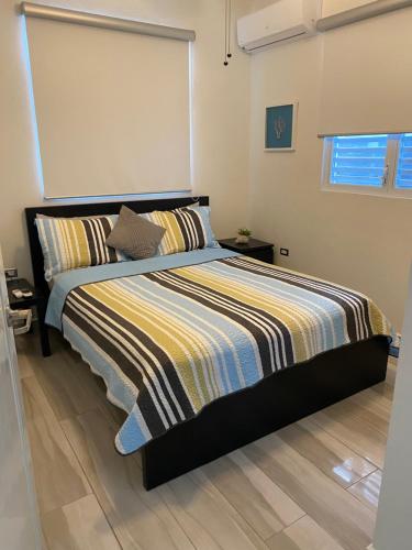 a bed with a striped comforter in a bedroom at Walk to the Beach 2Min, Cozy, Boutique, Pool, Palmeras Del Mar Isabela in Isabela