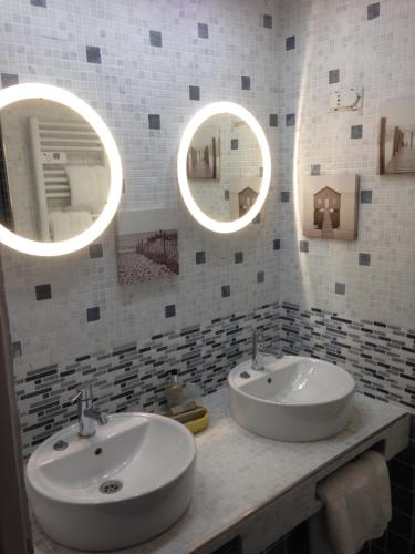 two sinks in a bathroom with three mirrors at L'Hôtel Le Cheval Noir in Moret-sur-Loing