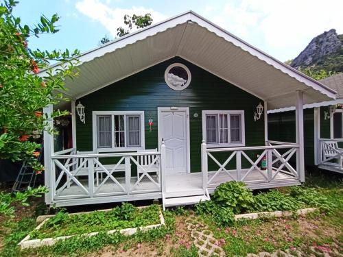 um chalé verde com um alpendre branco e uma porta em Lukkies Lodge Cirali em Cirali