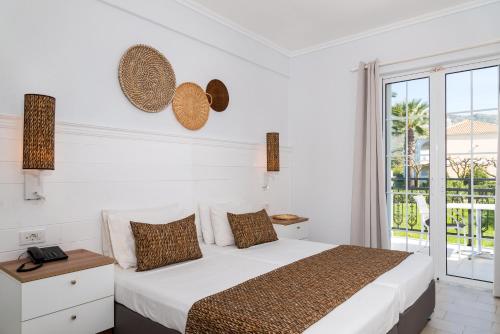 Sirocco Hotel في مدينة زاكينثوس: غرفة نوم بيضاء مع سرير ونافذة كبيرة