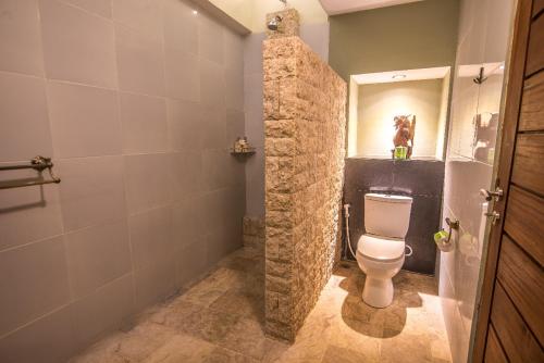 a bathroom with a toilet and a stone wall at Bali Santi Bungalows in Candidasa