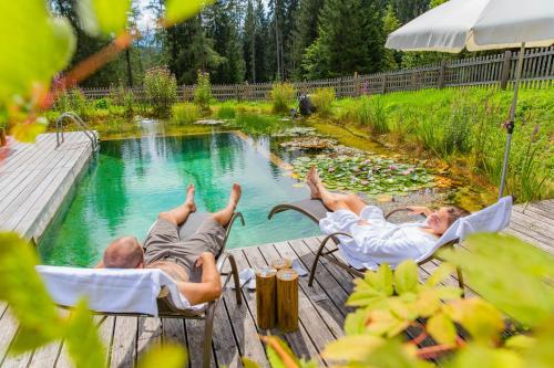 two men laying in chairs in a swimming pool at Hotel Lindenhof in Ramsau am Dachstein