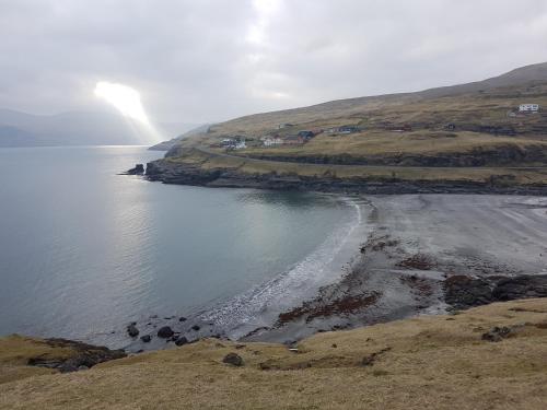 a body of water with a beach and houses on a hill at Stykkjastova - view and positioning in Kvívík