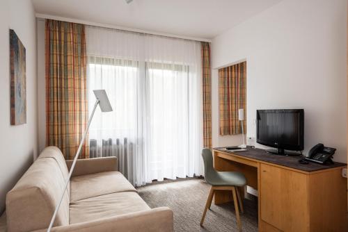 a hotel room with a couch and a desk with a television at Hotel Lindenhof Hubmersberg in Pommelsbrunn