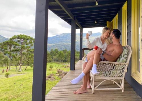 a man and a woman sitting on the porch of a house at Cabana Monte - Pousada Colina dos Ventos in Urubici