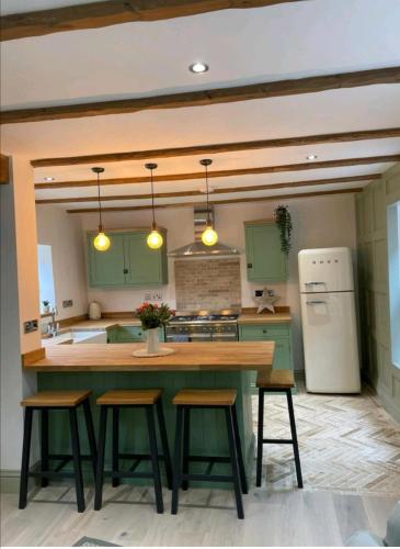 a kitchen with green cabinets and a kitchen island with stools at Ferry Lane Cottage in King's Lynn