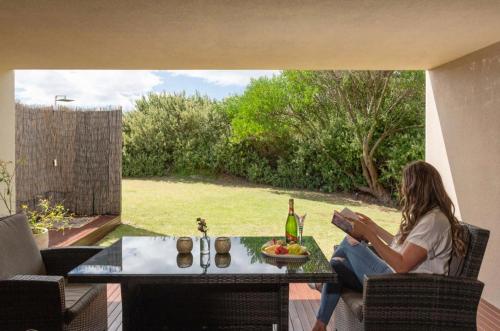 a woman sitting at a table reading a book at Amarè Beachside Luxury in Turners Beach