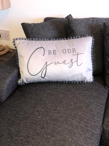 a pillow that says be our guest on a couch at Driftwood Apartment - Skegness in Skegness