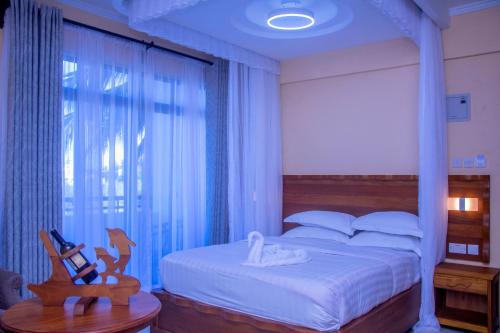 a bedroom with a white bed with a large window at Hotel Comster Mtwapa in Mtwapa