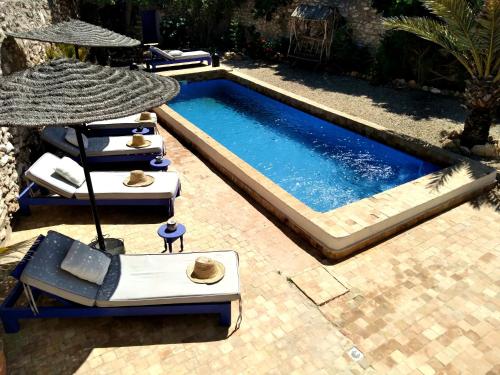 a swimming pool with two lounge chairs and an umbrella at Dar Mayssoun in Ghazoua