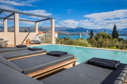a swimming pool with four cushioned chairs on the edge of a house at Ionian Village in Lixouri