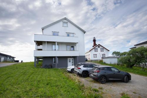 two cars parked in front of a white house with a lighthouse at Apt 101 - Andenes Whale Safari Apartments in Andenes