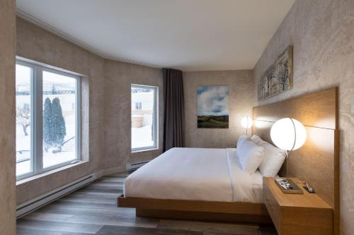 a bedroom with a large bed and two windows at Hotel Chateau Bromont in Bromont