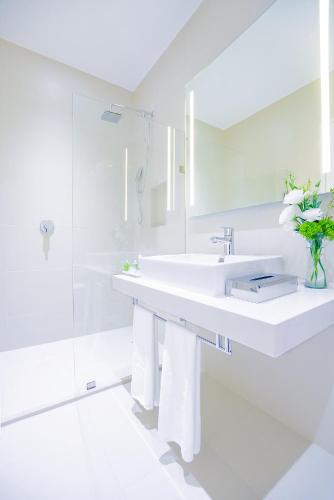 a white bathroom with a sink and a vase of flowers at NH Puebla FINSA in Puebla