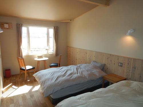a bedroom with two beds and a window and a table at Meiji no Okano Yado in Biei