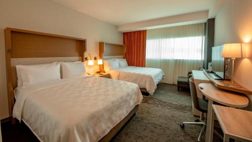 Holiday Inn & Suites - Merida La Isla, an IHG Hotel في ميريدا: غرفة فندقية بسريرين ومكتب