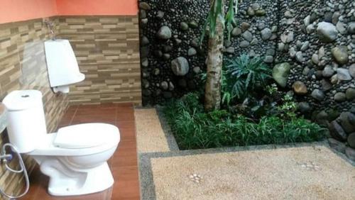 a bathroom with a toilet in front of a stone wall at Kampoeng Tourist Homestay in Licin