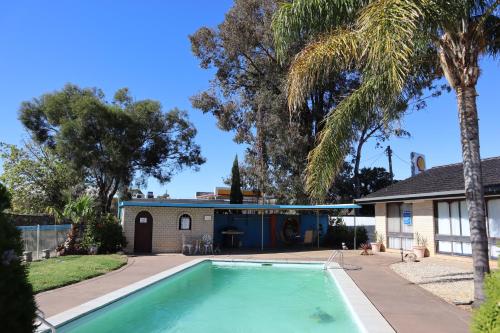 a swimming pool in front of a house with a palm tree at Capri Motel in Balranald