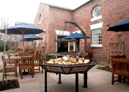 a grill in a patio with tables and umbrellas at The Swan at Tarporley in Tarporley