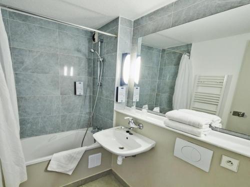 ein Badezimmer mit einem Waschbecken, einer Badewanne und einem Spiegel in der Unterkunft Kyriad Chantilly Sud - Luzarches in Chaumontel
