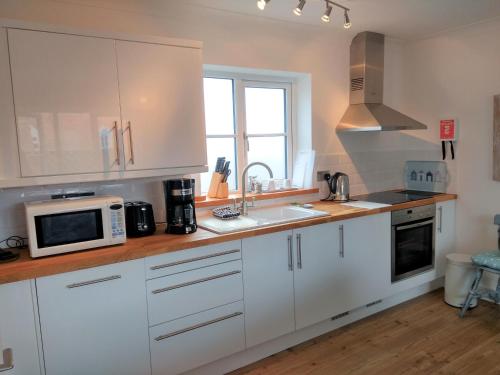 a kitchen with white cabinets and a microwave at AnchorageWells Harbour Apartment in Wells next the Sea