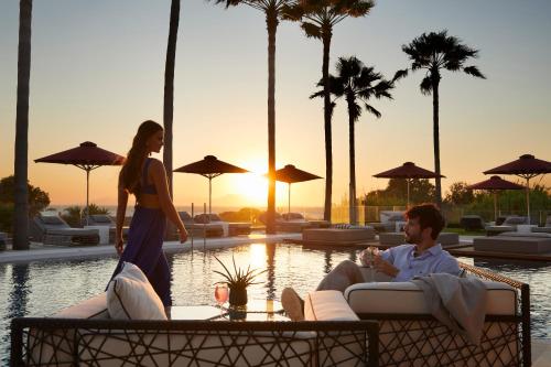 a woman walking past a man sitting in a chair next to a pool at Aqua Blu Boutique Hotel & Spa, Adults Only- Small Luxury Hotels of the World in Kos