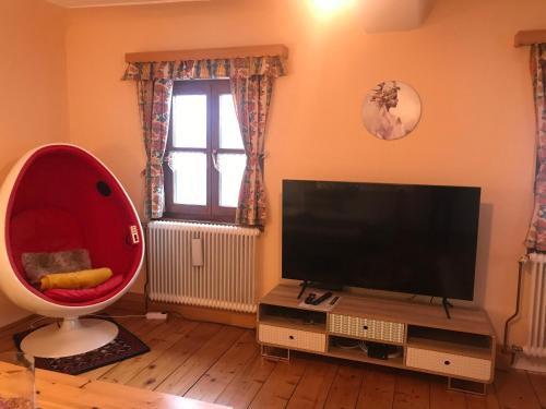ein Wohnzimmer mit einem TV und einem großen roten Stuhl in der Unterkunft Weichselboden, Alte Schule in Weichselboden