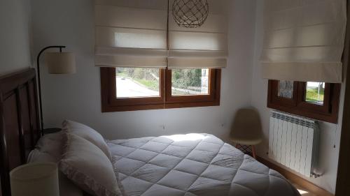 a bedroom with a white bed and two windows at Apartamentos La Glera Biescas in Biescas