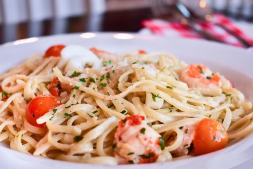 a white plate of pasta with shrimp and tomatoes at Sinclair Guest House in Abuja