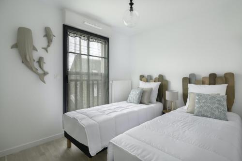 une chambre blanche avec deux lits et une fenêtre dans l'établissement Face à la mer, bel appartement pour 6, à Pléneuf-Val-André