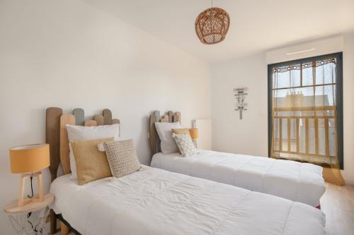 Dos camas en una habitación blanca con ventana. en Bel appartement pour 4 à 50m de la plage, en Pléneuf-Val-André